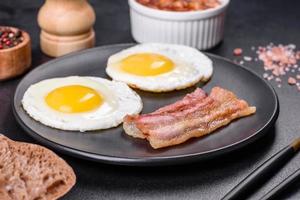 English breakfast with fried eggs, bacon, beans, tomatoes, spices and herbs photo