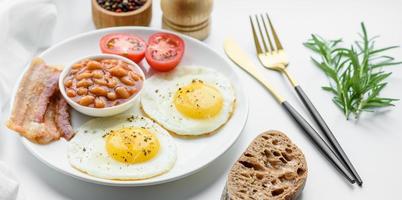 English breakfast with fried eggs, bacon, beans, tomatoes, spices and herbs photo