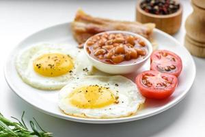 English breakfast with fried eggs, bacon, beans, tomatoes, spices and herbs photo
