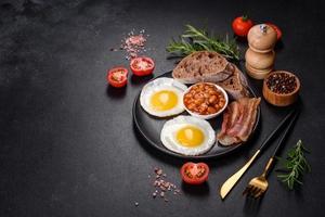 English breakfast with fried eggs, bacon, beans, tomatoes, spices and herbs photo