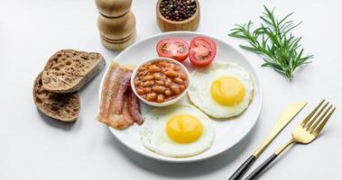 English breakfast with fried eggs, bacon, beans, tomatoes, spices and herbs photo