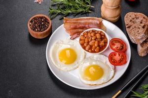 English breakfast with fried eggs, bacon, beans, tomatoes, spices and herbs photo