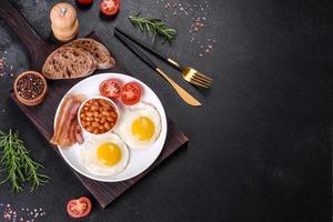 English breakfast with fried eggs, bacon, beans, tomatoes, spices and herbs photo