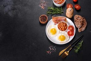 English breakfast with fried eggs, bacon, beans, tomatoes, spices and herbs photo