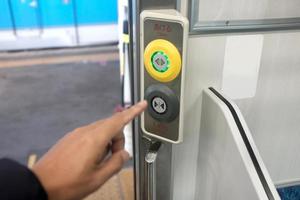 primer plano de una mano presionando el botón de cierre en el costado de la entrada de la puerta del tren foto