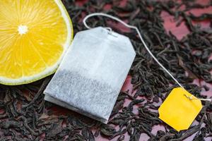 Tea bag with a yellow label and fresh lemon lie on the leaves of black tea