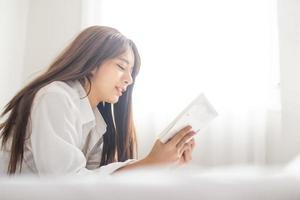 retrato joven sonrisa feliz hermosa mujer asiática relajarse dormitorio. mujer joven leyendo un libro por la mañana foto