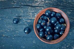 Black currant in a ceramic bowl on wooden background photo