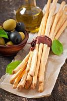 Grissini bread sticks with ham, olives, basil on old wooden background photo