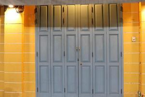 Old style gray painted wood doors are closed and light from lamp, color of wall beside the door is yellow, Thailand. photo