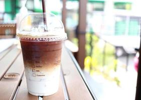 Ice coffee two layer of coffee and milk in closed plastic glass with straw on dark brown table and blur bright background in Thailand. photo