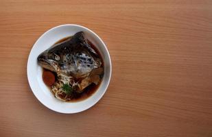 Boiled salmon head with soy sauce or Salmon kabutoni on white round dish and brown wood background. photo