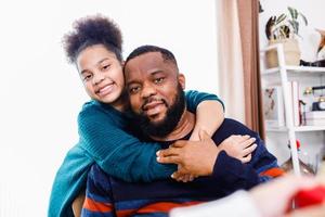 padre afroamericano e hija usando suéteres abrazándose y divirtiéndose. familia afroamericana foto