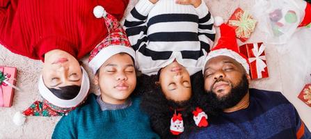 familia afroamericana en tema navideño. feliz familia afroamericana de cuatro personas que se unen en el suelo juntos. foto