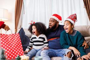 familia afroamericana sorprendida con un regalo el día de navidad. Feliz Navidad. foto