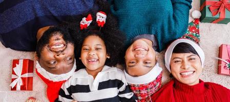 familia afroamericana en tema navideño. feliz familia afroamericana de cuatro personas que se unen en el suelo juntos. foto