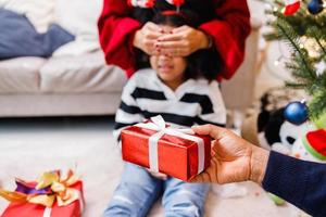 familia afroamericana sorprendiendo con un regalo el día de navidad. Feliz Navidad. foto