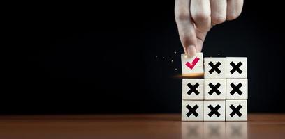 right and wrong icon on wooden cube with man hand select correct icon on dark background . photo