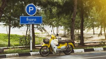 A bright yellow Honda motorcycle, Super cub, is parked next to a traffic sign designated as a parking lot. Tang book in Thai means parking.