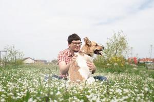 Happy man sitting with mixed breed shepherd dog on green grass in spring flowers photo