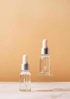 Glass dropper bottles with a pippette with black rubber tip on glass podium and beige background, mockup design photo