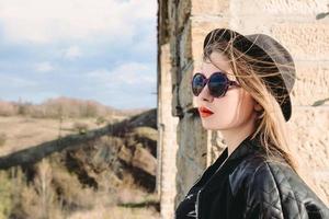 Stylish hipster woman traveler in sunglasses and black hat by the old bridge viaduct. Traveling, Europe, fashion, style concept photo