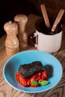 lomo de cerdo al horno marinado en tinta de sepia con tomates rojos y albahaca en plato azul foto
