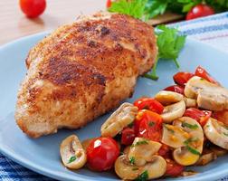 Chicken fillet in crispy breadcrumbs garnished with mushrooms and tomatoes photo