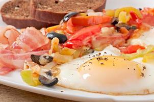 Breakfast - fried eggs with bacon, tomatoes, olives and slices of cheese photo