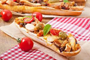 Big sandwich with roasted vegetablesn and chicken with cheese and basil on old wooden background photo