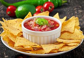 Mexican nacho chips and salsa dip in  bowl on  wooden background photo