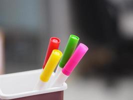 many magic pen red, pink, yellow, green color in brown plastic box, blurred of notebook background photo