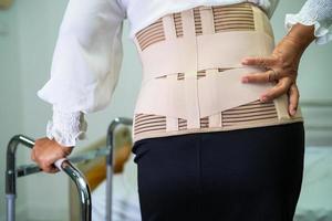 Asian lady patient wearing back pain support belt for orthopedic lumbar with walker. photo