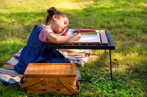 A little girl is sitting on the cloth and painted on the paper placed on a table photo