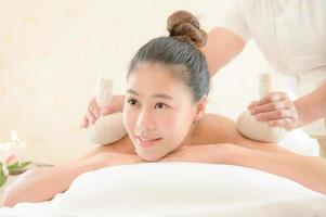 A beautiful Asian woman is laid back and relaxing, the masseuse uses a hot herbal compress in a spa shop photo