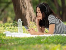 Beautiful Asian woman lying in the garden and using a mobile phone, Can search for music or shop online on the internet photo
