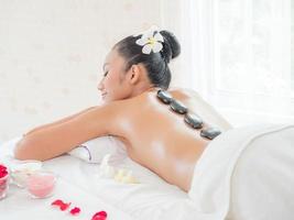 una hermosa mujer asiática se relaja en una tienda de spa cuando una experta masajista le coloca una piedra caliente en la espalda foto
