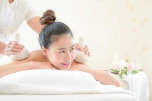 una hermosa mujer asiática está relajada y relajada, la masajista usa una compresa de hierbas calientes en una tienda de spa