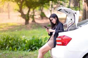 A beautiful Asian woman sitting in the back of a car and using a mobile phone to work outside of the office. The concept of working at home during the corona virus epidemic