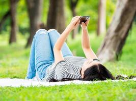 hermosa mujer asiática tendida en el jardín y usando un teléfono móvil, puede buscar información o comprar en línea en Internet foto