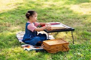 A little girl is sitting on the cloth and painted on the paper placed on a table photo