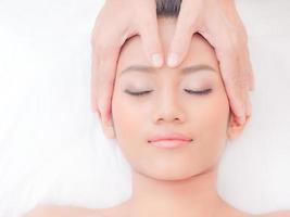 A beautiful Asian woman closes her eyes, relaxes in a spa shop with a facial massage from a professional masseuse photo