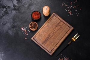 Brown rectangular wooden cutting board with salt and spices on a dark concrete background photo