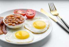 desayuno inglés con huevos fritos, tocino, frijoles, tomates, especias y hierbas