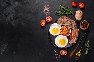 English breakfast with fried eggs, bacon, beans, tomatoes, spices and herbs photo