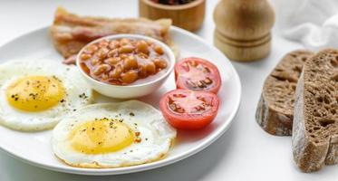 English breakfast with fried eggs, bacon, beans, tomatoes, spices and herbs photo