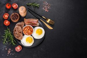 English breakfast with fried eggs, bacon, beans, tomatoes, spices and herbs photo