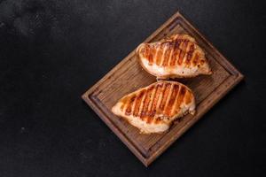 Delicious fresh grilled chicken fillet with spices and herbs on a dark concrete background photo