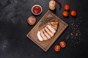 Delicious fresh grilled chicken fillet with spices and herbs on a dark concrete background photo