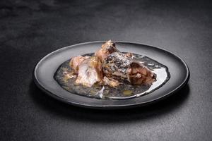 Canned sardine in oil on a black round plate against a dark concrete background photo